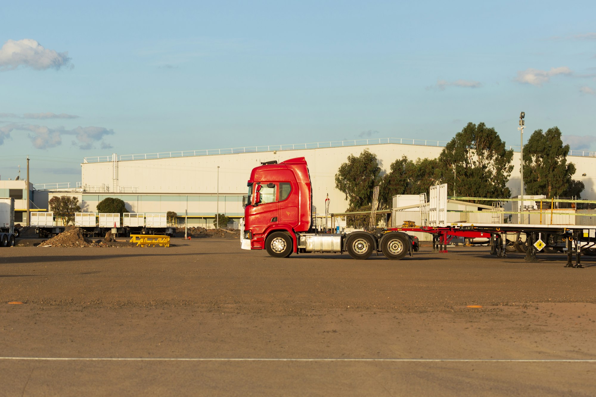 Red semi tractor and flatbed trailers in front of a warehouse